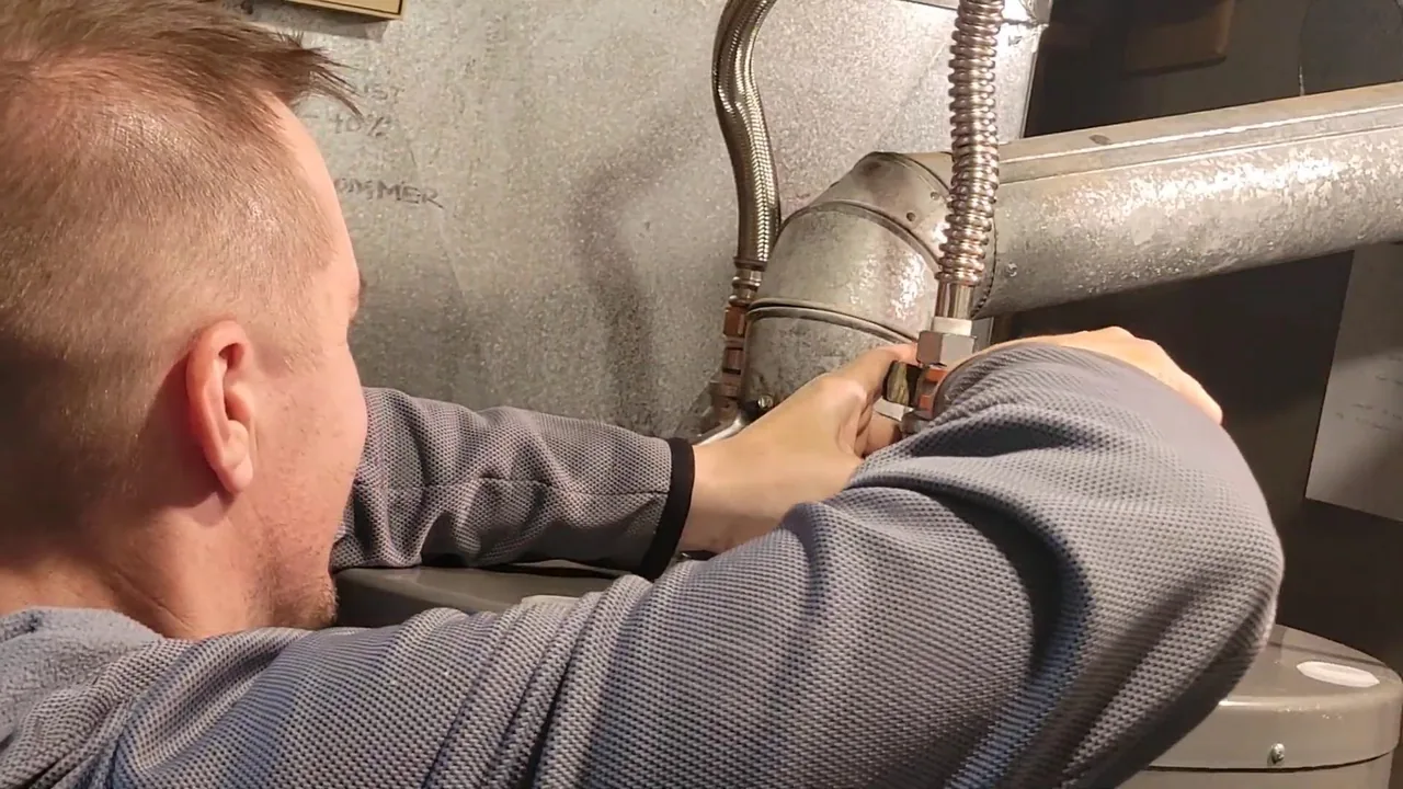 Plumber leaning in to connect a flexible line at the top of a water heater.